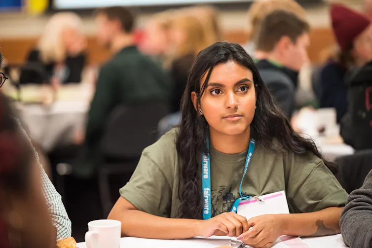 A person listens at a roundtable while people are seen in the background.