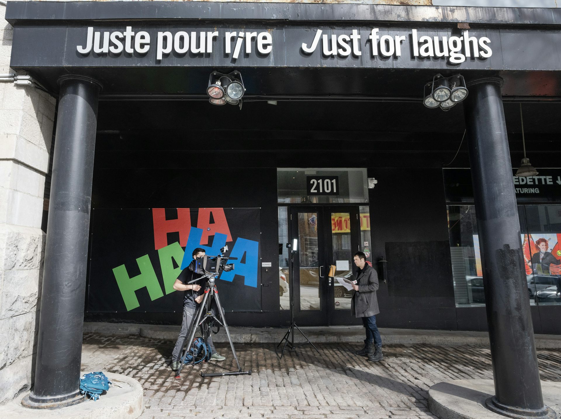 A person with a camera seen shooting someone with microphone in front of storefront with the sign Juste Pour Rire Just for Laughs.
