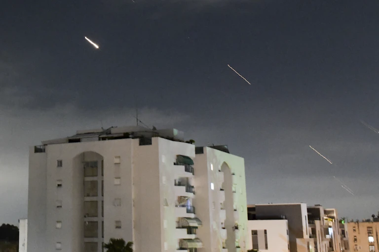 Streaks of light flash across the sky above buildings.