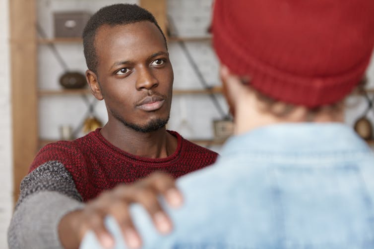 A young man has his back to the camera with his hand on the shoulder of another young man.