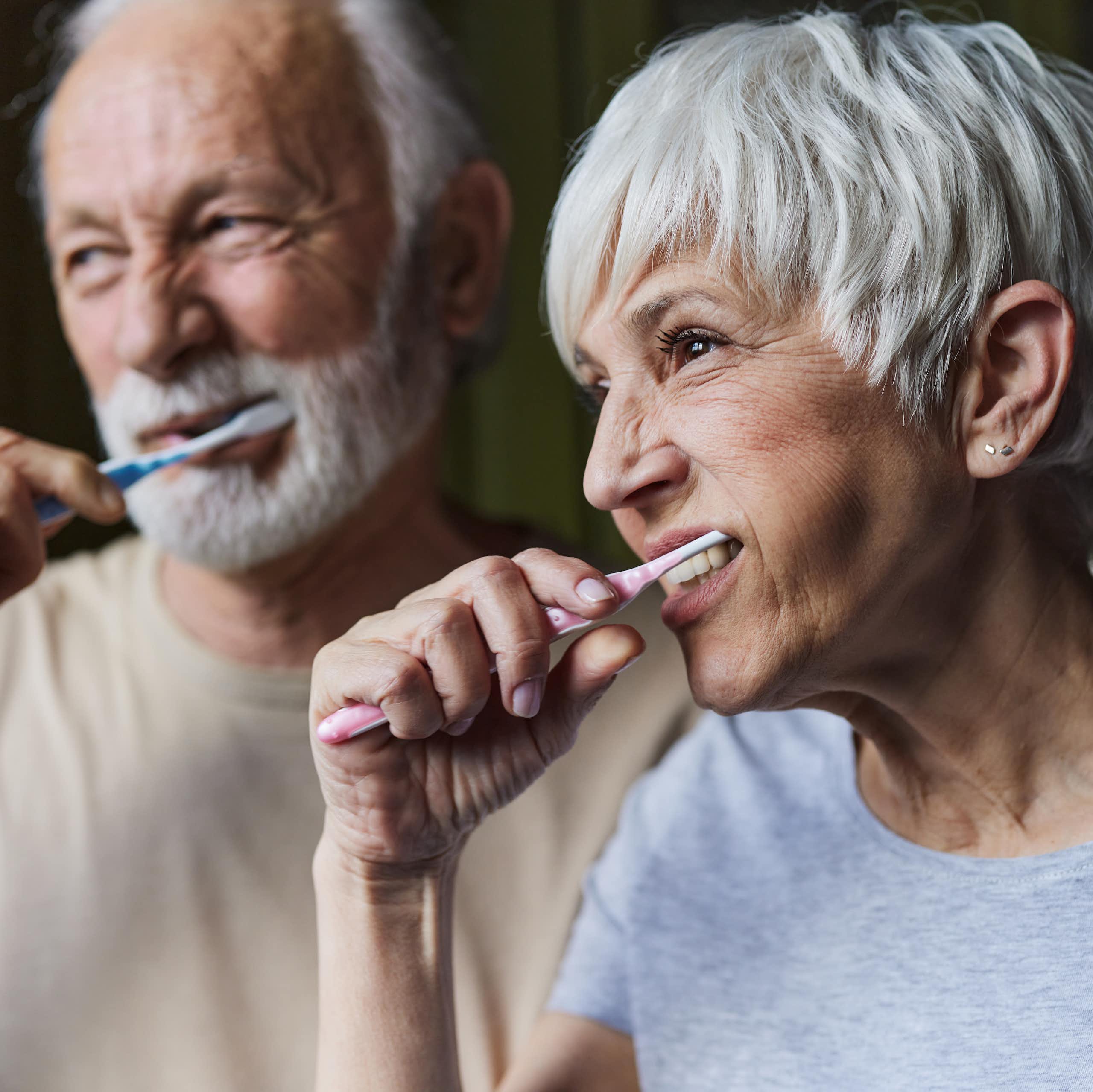 Older man and older  woman brush their teeth.