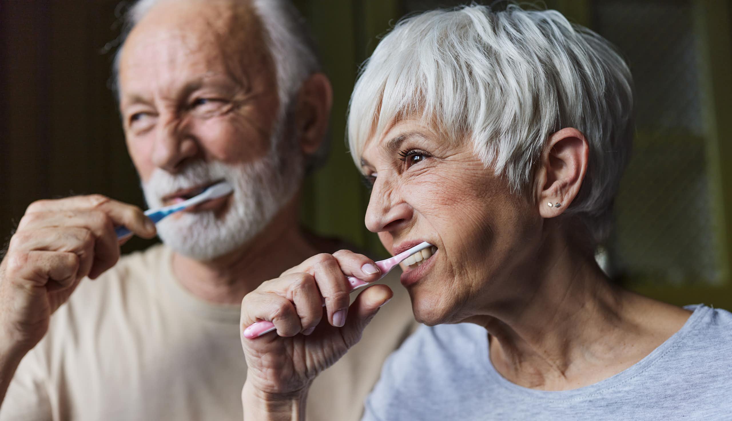 Older man and older  woman brush their teeth.