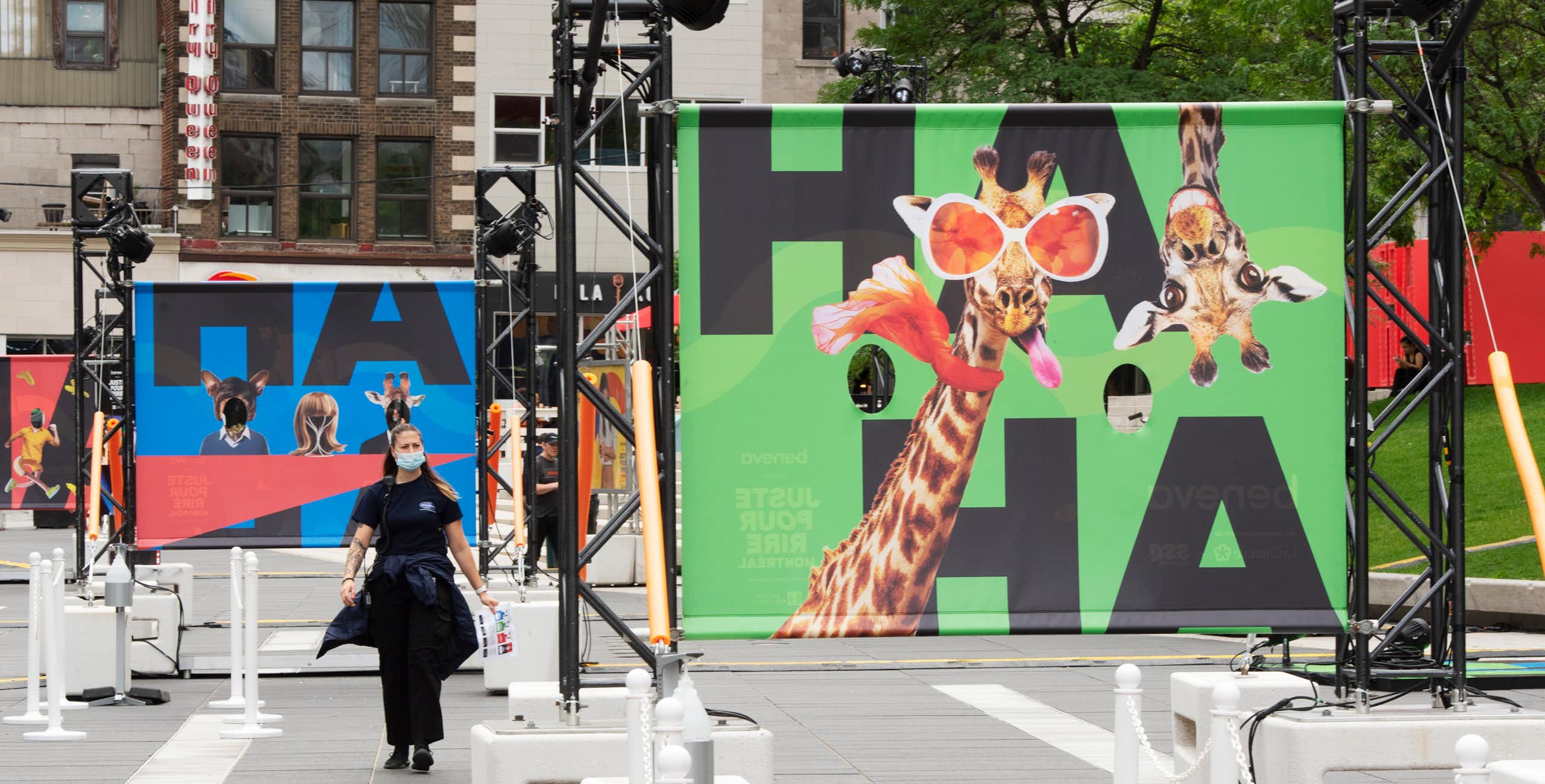A sign with a giraffe in funny glasses sticking tongue out says 'ha ha' and a person walks past.