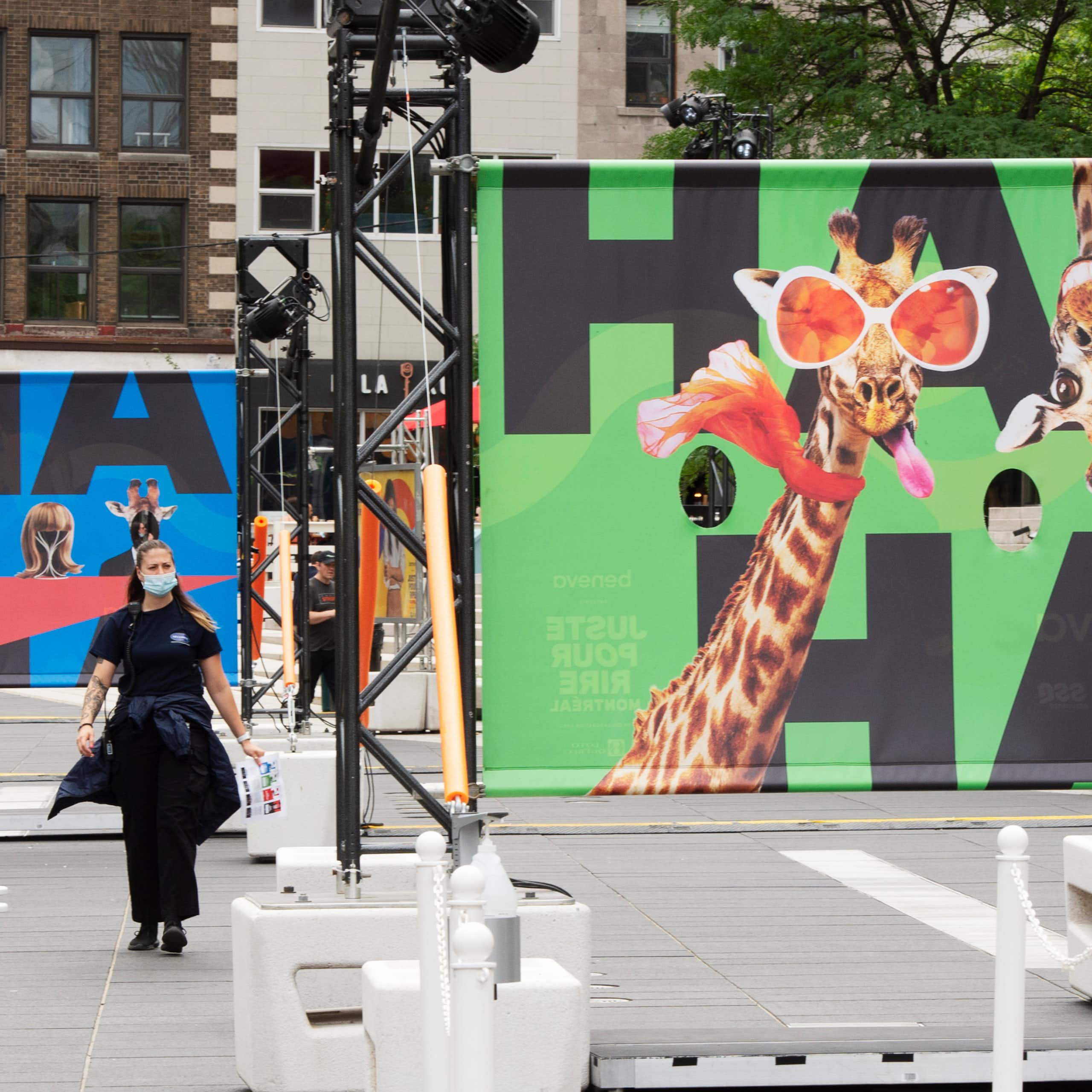 A sign with a giraffe in funny glasses sticking tongue out says 'ha ha' and a person walks past.