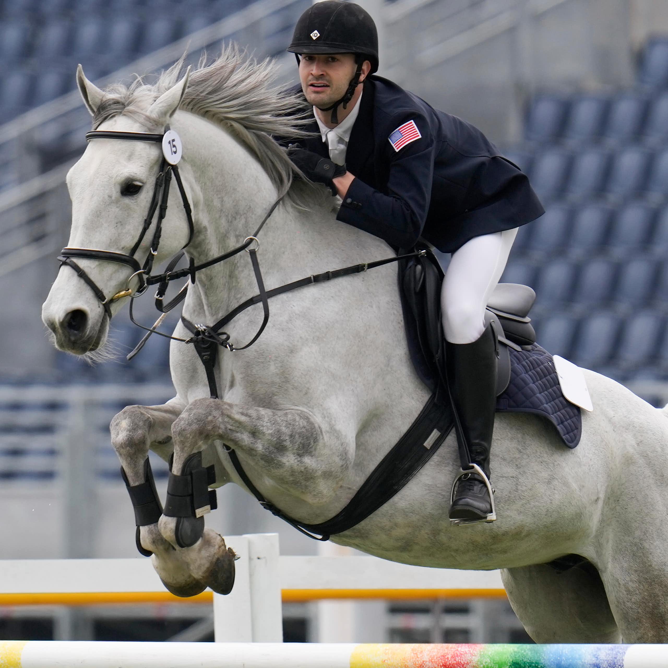 A horseback rider leans forward in the saddle as a gray horse jumps over an obstacle