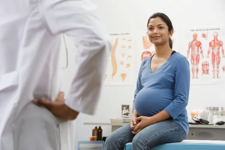 Une femme enceinte dans un cabinet médical avec un agent de santé en blouse blanche vu de dos
