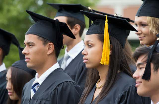Male and female students of different ethnic backgrounds don black graduation caps and gowns. 