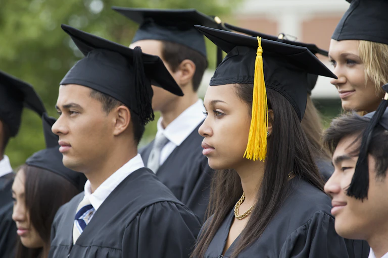 Male and female students of different ethnic backgrounds don black graduation caps and gowns.