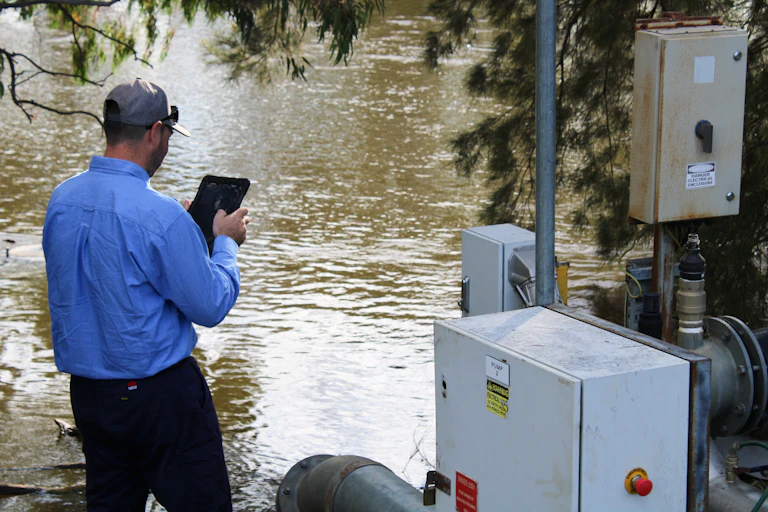 Rear view of a man inspecting an irrigation pump on a river