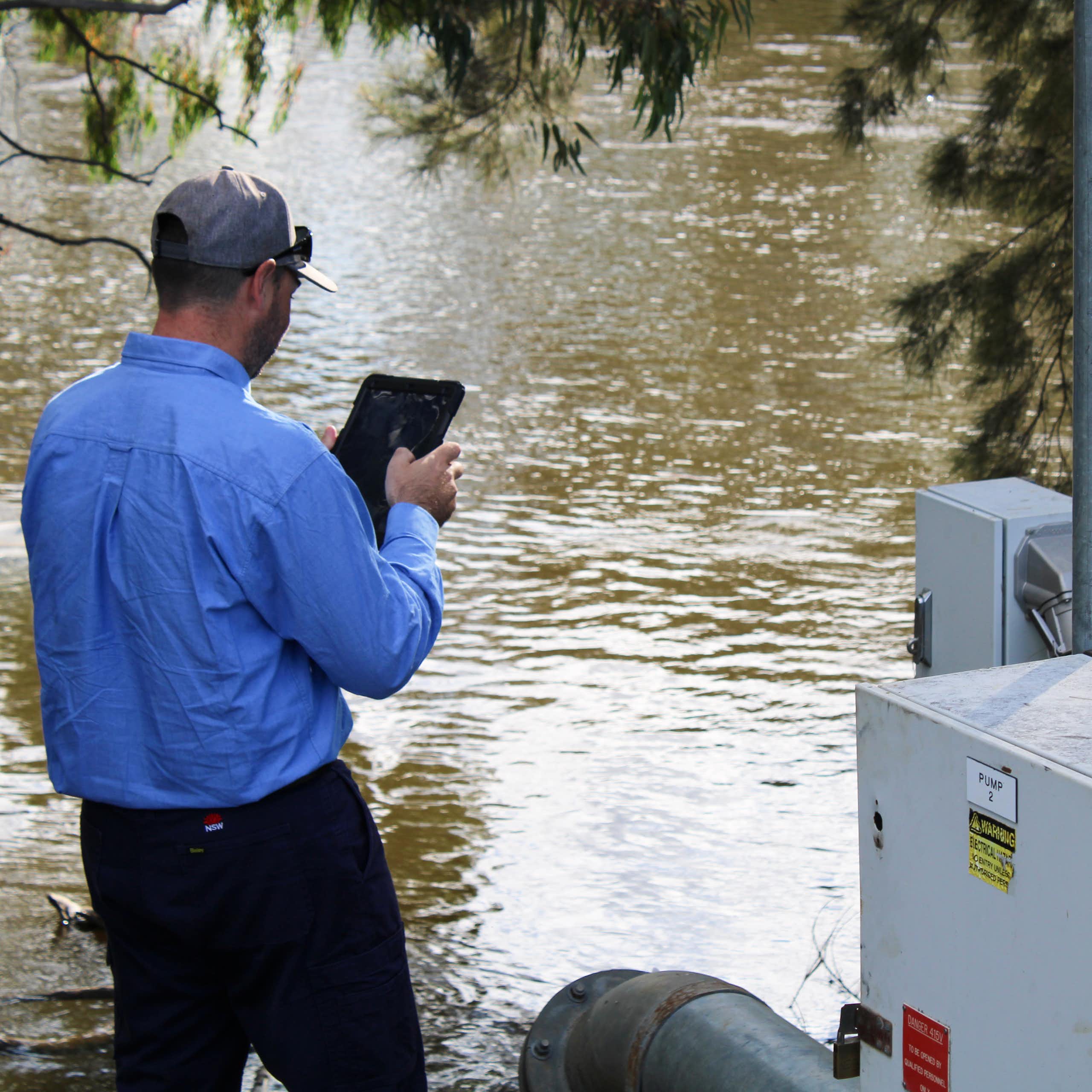 Rear view of a man inspecting an irrigation pump on a river