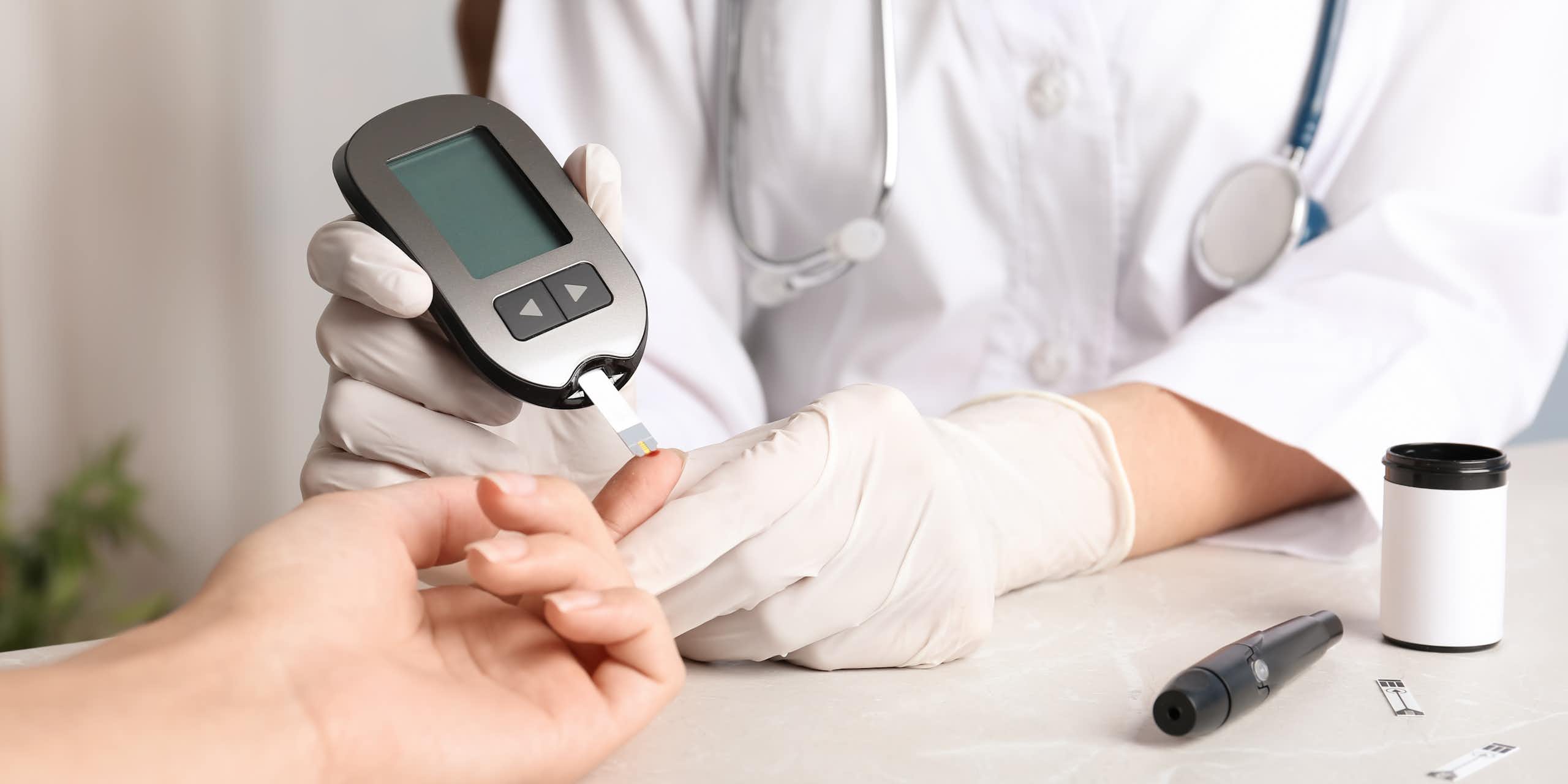 Gloved hands of a health-care worker testing a patient's finger with a glucose meter