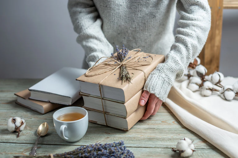 Unas manos de mujer apoyan tres libros envueltos para regalo en una mesa.