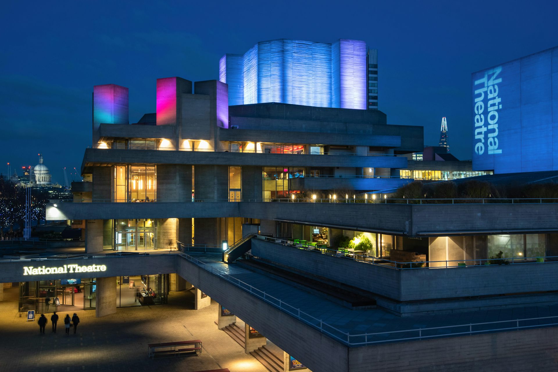 A concrete building on London's South Bank - the National Theater - lit up red and blue at night.