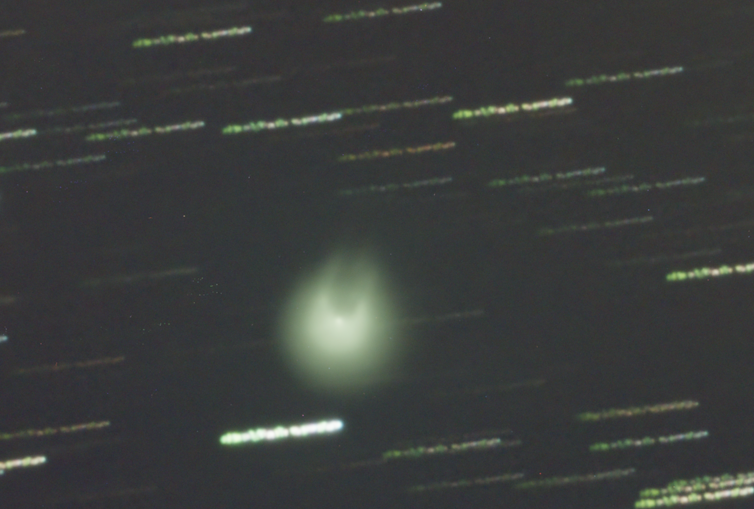 A fuzzy green blob in the night sky with two horn-like protrusions.