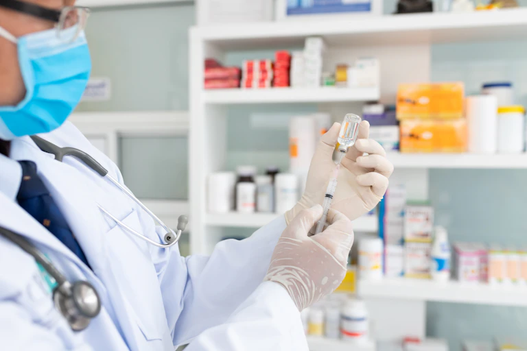 A pharmacist fills a syringe with vaccine fluid.