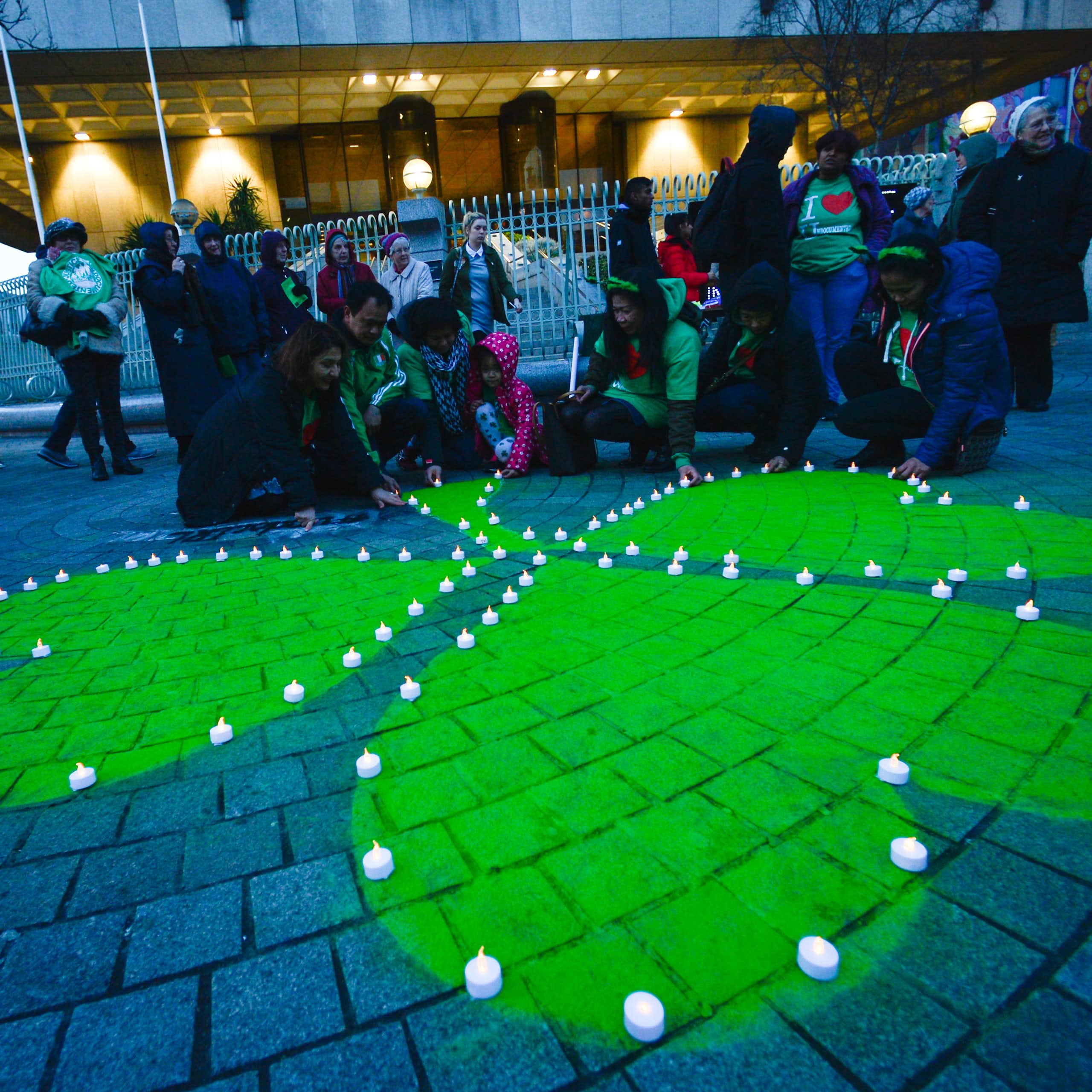 A green shamrock is painted on stone pavement surrounded by people in 'I heart Ireland' T-shirts.