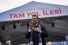 A dark-haired man in glasses speaks at a rally.