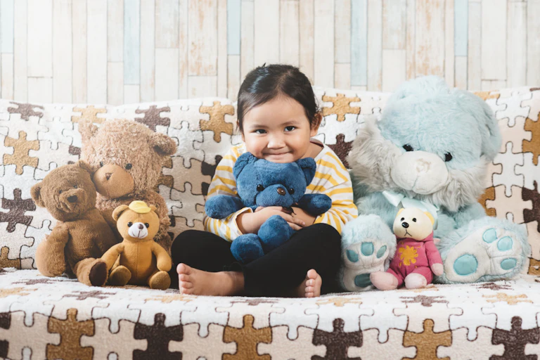 Une petite fille sur un canapé entourée de ses peluches