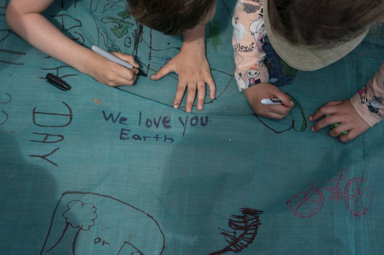 Hands seen writing 'I love you' on a green fabric.