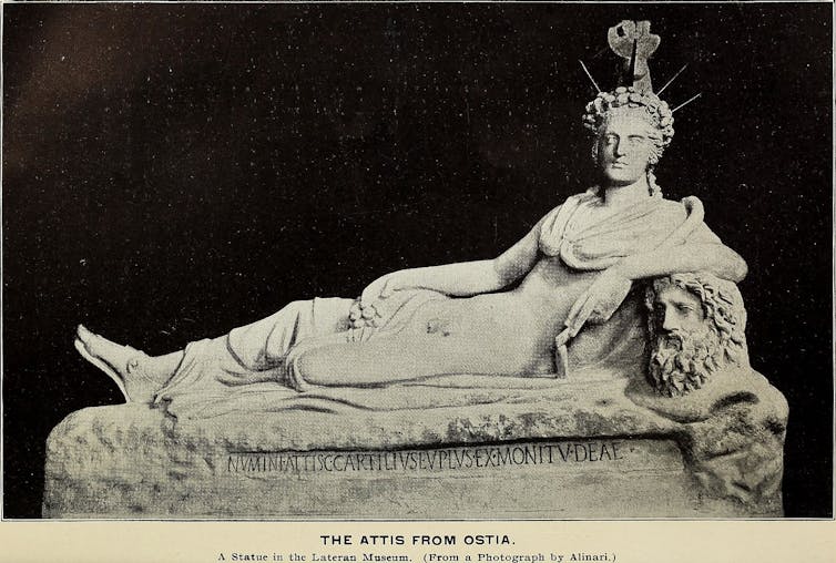 Sculpture of a reclining figure with an ornate crown around which rays of sunshine shine.  A piece of clothing covers the upper body but exposes the genitals.