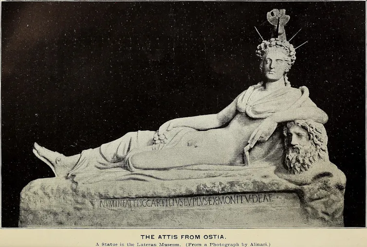 Sculpture d’une figure allongée portant une couronne élaborée entourée de rayons de soleil. Un vêtement recouvre le haut du corps mais laisse apparaître les parties génitales