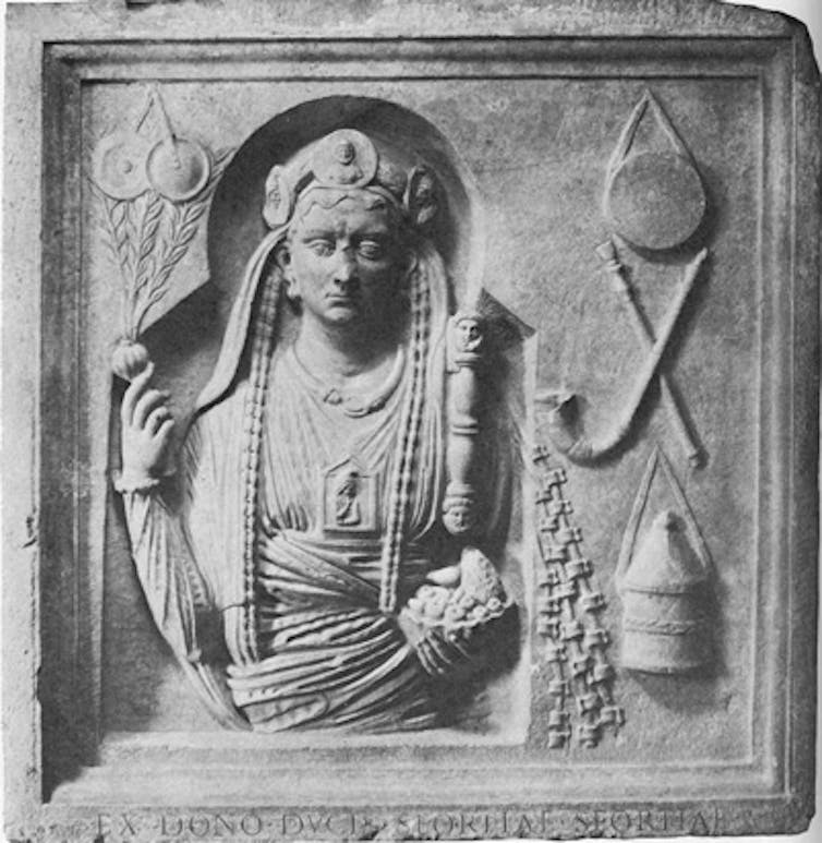 A decorated figure with several objects engraved on one side, such as a musical instrument and a box.