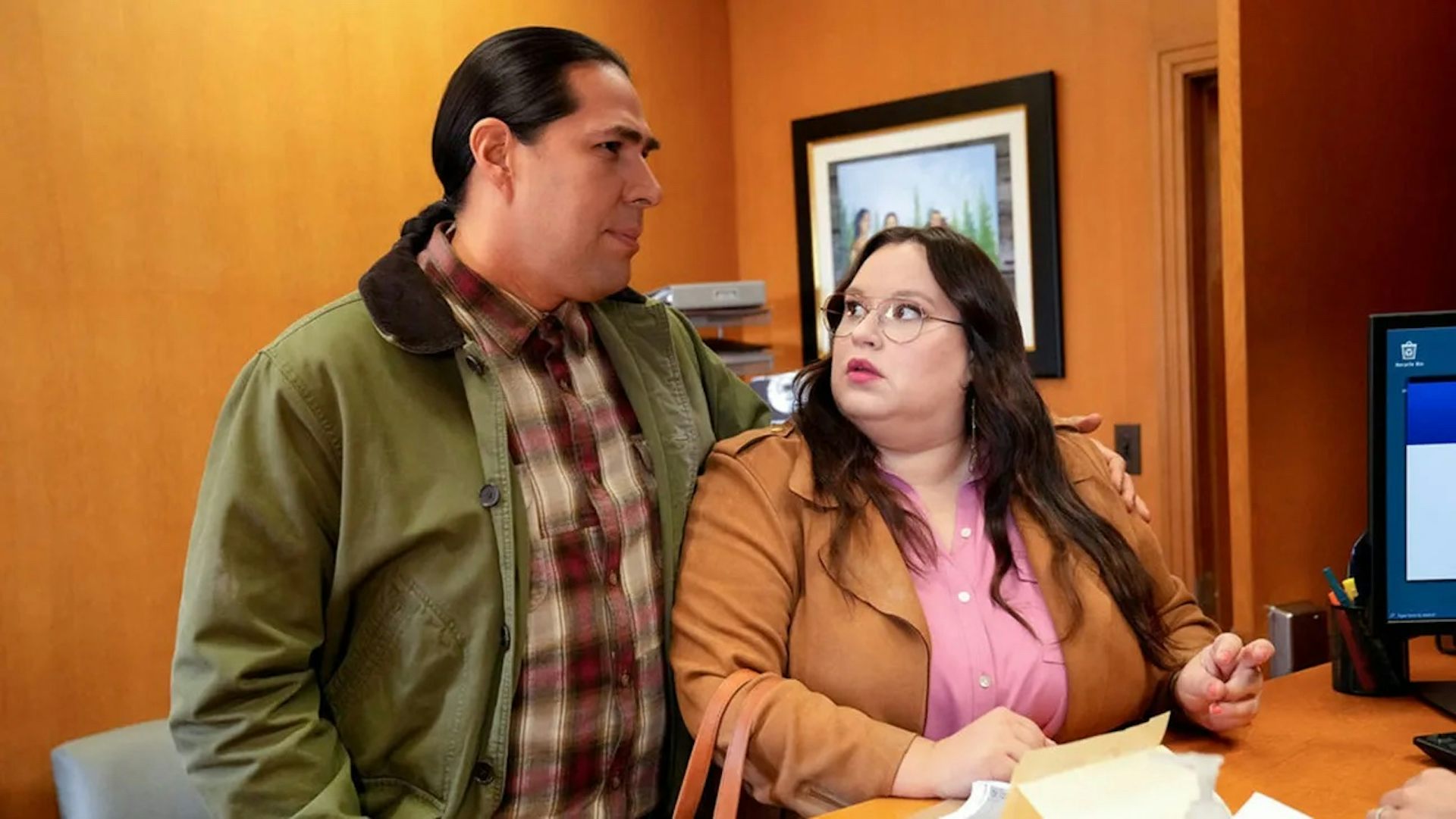 Man wearing olive green jacket side hugs a woman wearing a brown-colored trench coat.