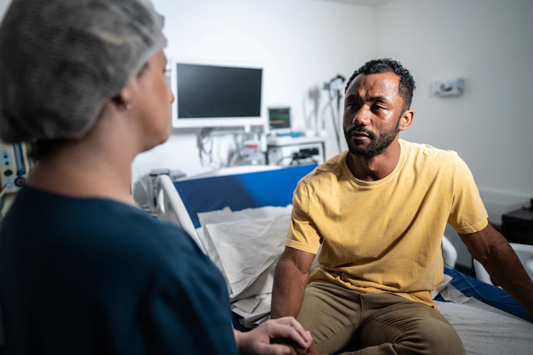 Over-the-shoulder shot of health care provider talking to a patient sitting on a hostpital bed