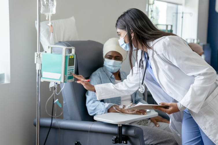 Health care provider adjusting an infusion pump while the patient sitting in a chair looks on