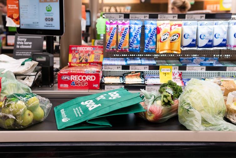 Groceries on a conveyor belt and snack foods displayed near the checkout counter in Woolworths.