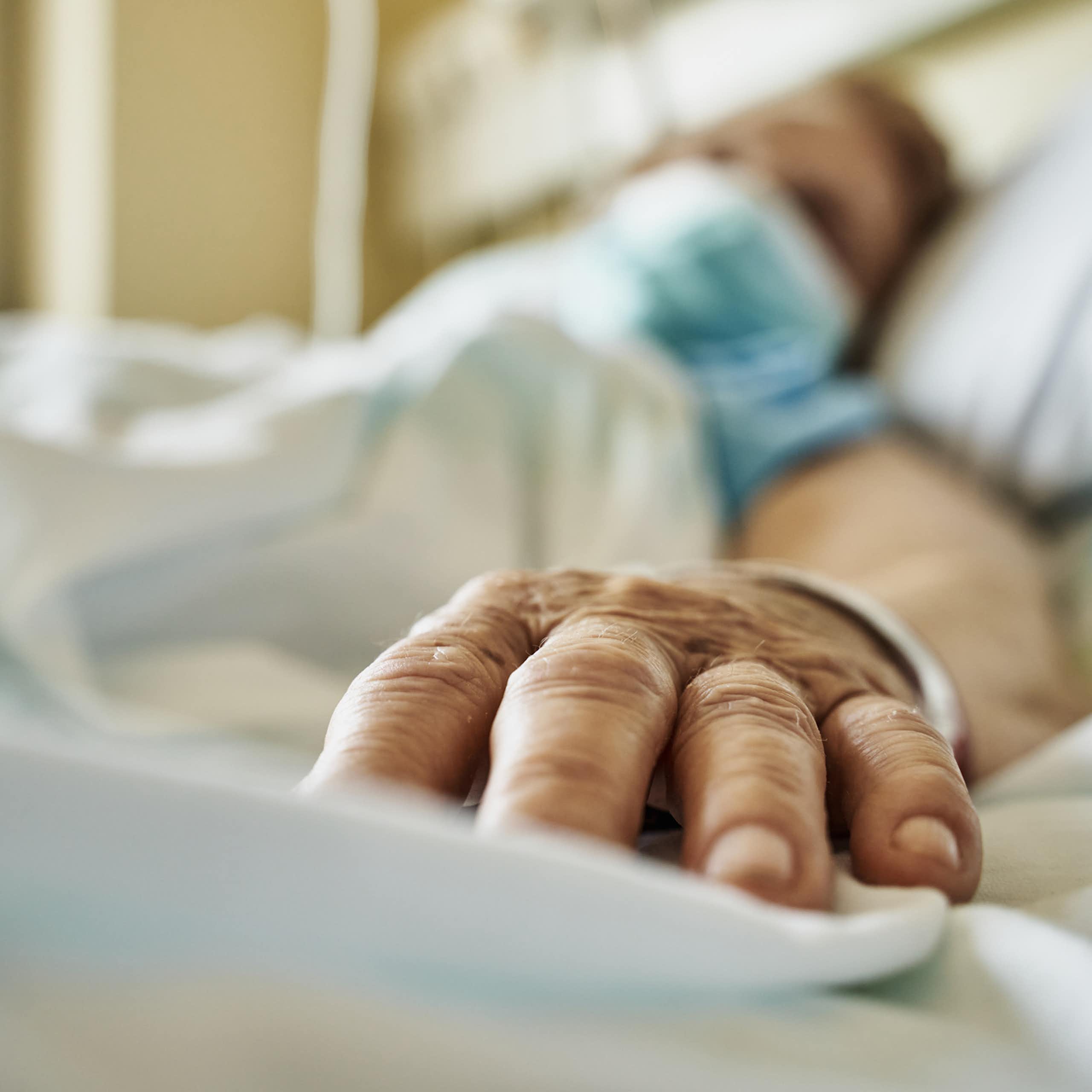 Paciente usando máscara deitado em uma cama de hospital, com a mão estendida em direção à câmera