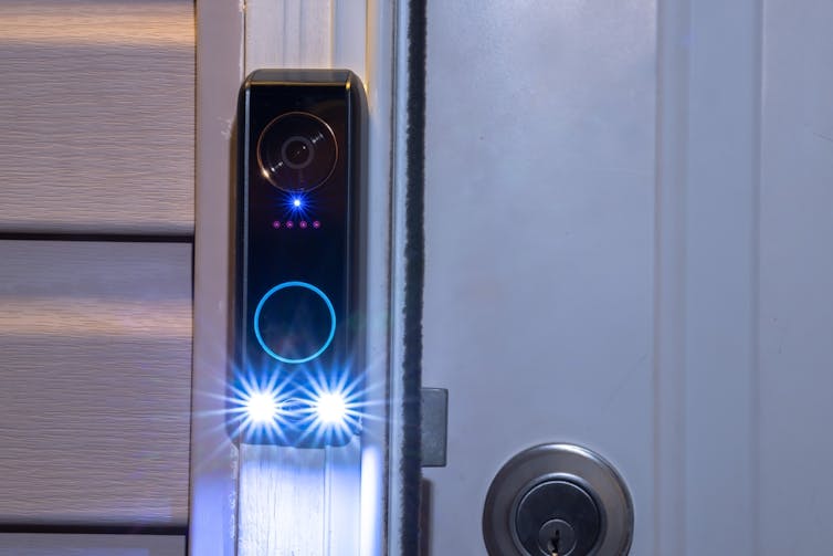 A doorbell device with blue and white lights glowing on it, indicating a camera is activated.