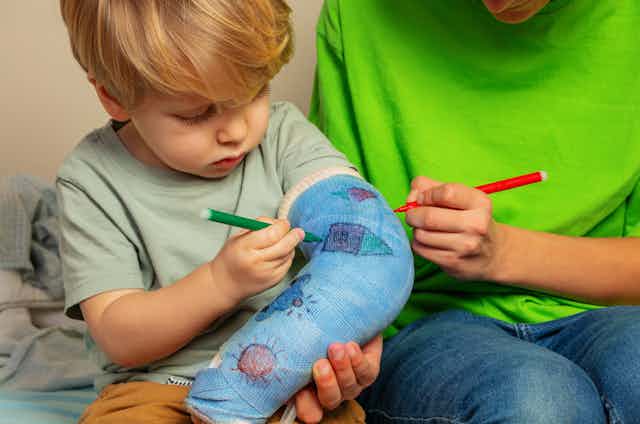 Boy with brother draw broken hand plaster cast painting childish drawings using felt-tip pen