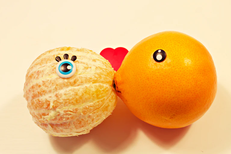 A peeled and an unpeeled orange kiss.