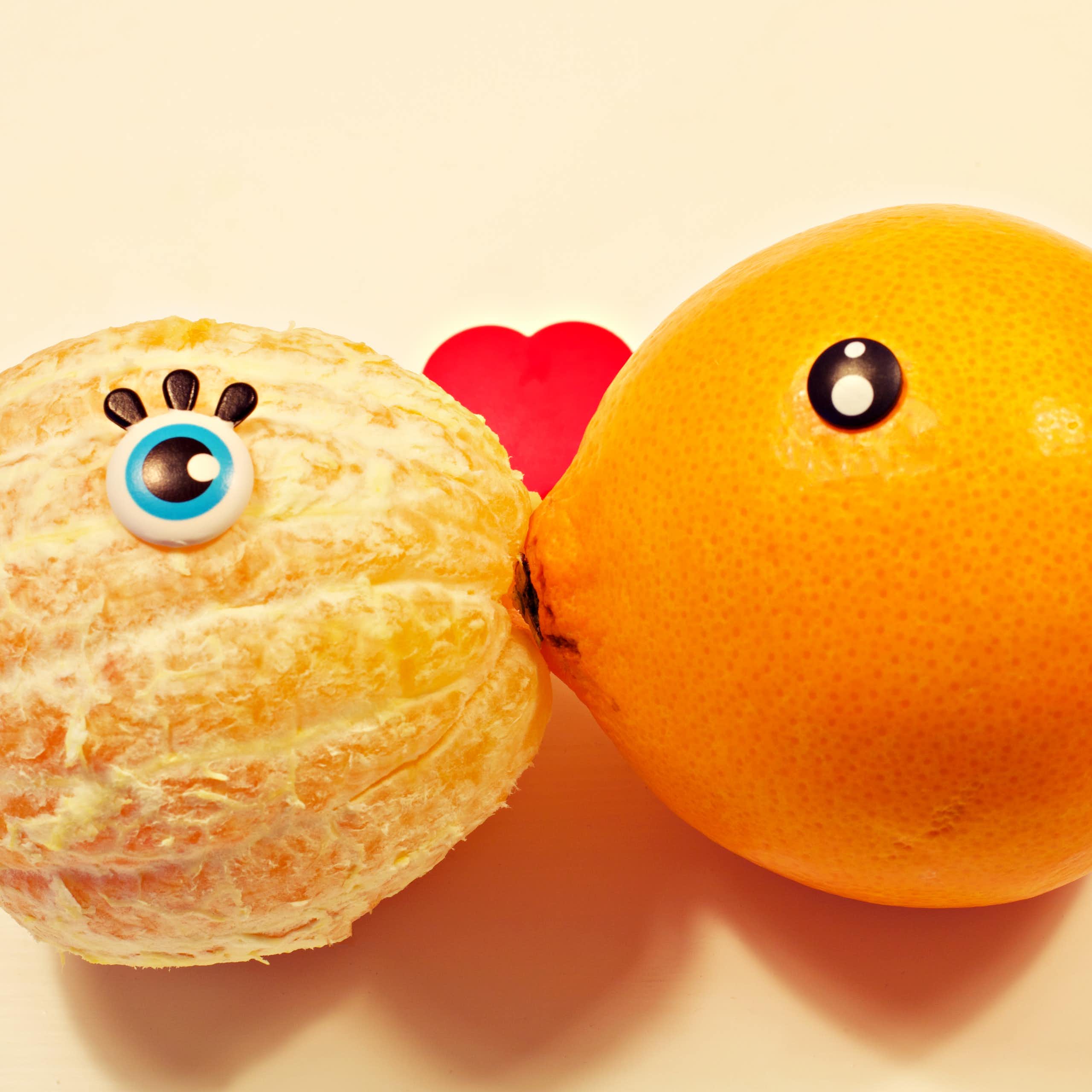 A peeled and an unpeeled orange kiss.
