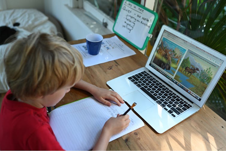 A boy sits at a desk with a computer and notepad.