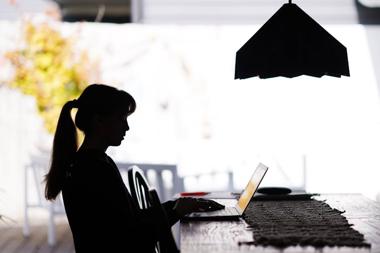 A teenage girl sits at a table working on a laptop.