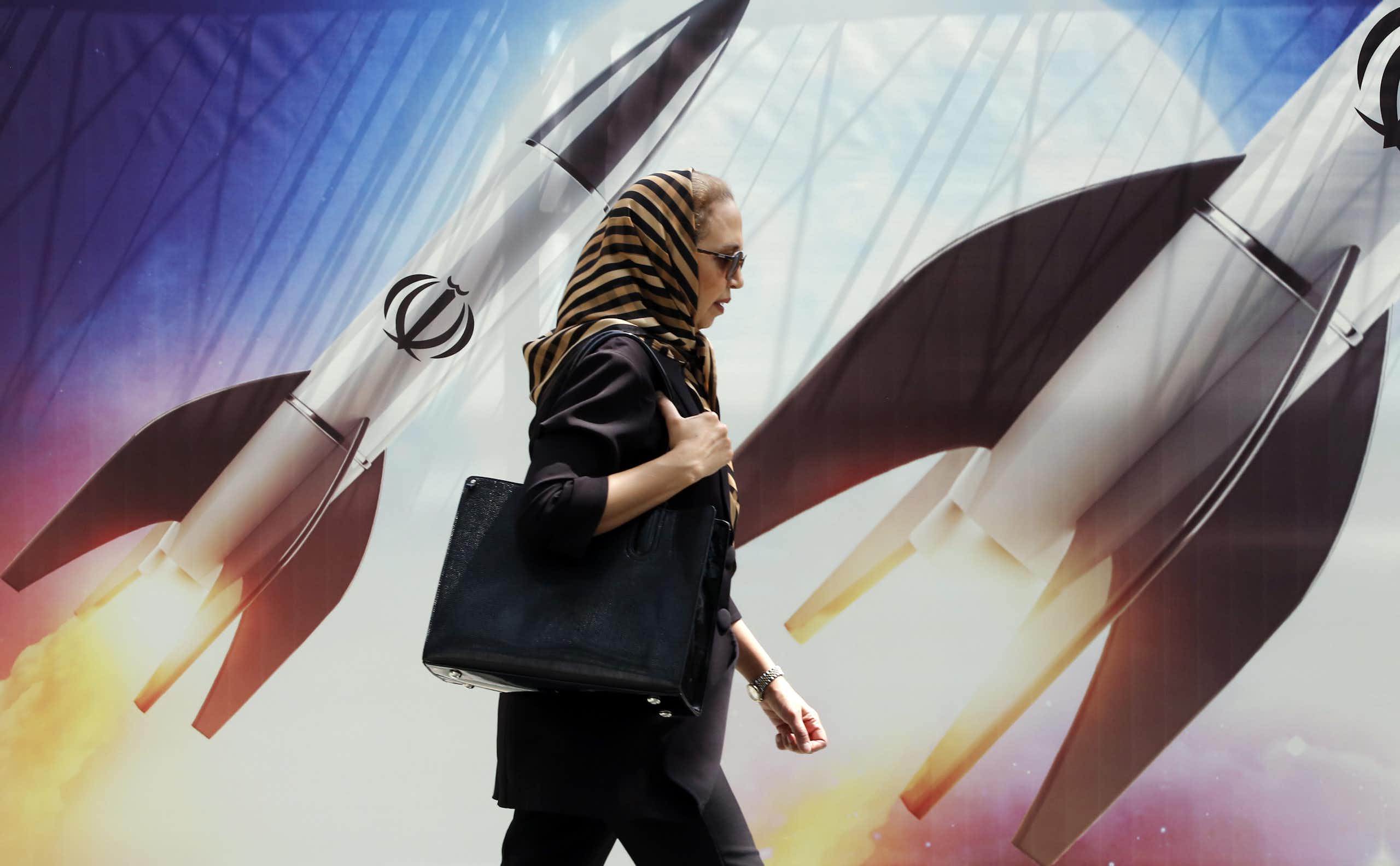 Woman walks past a billboard showing Iranian missiles in flight