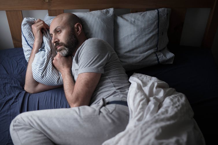 Photo of a sad-looking middle-aged man lying in bed alone.