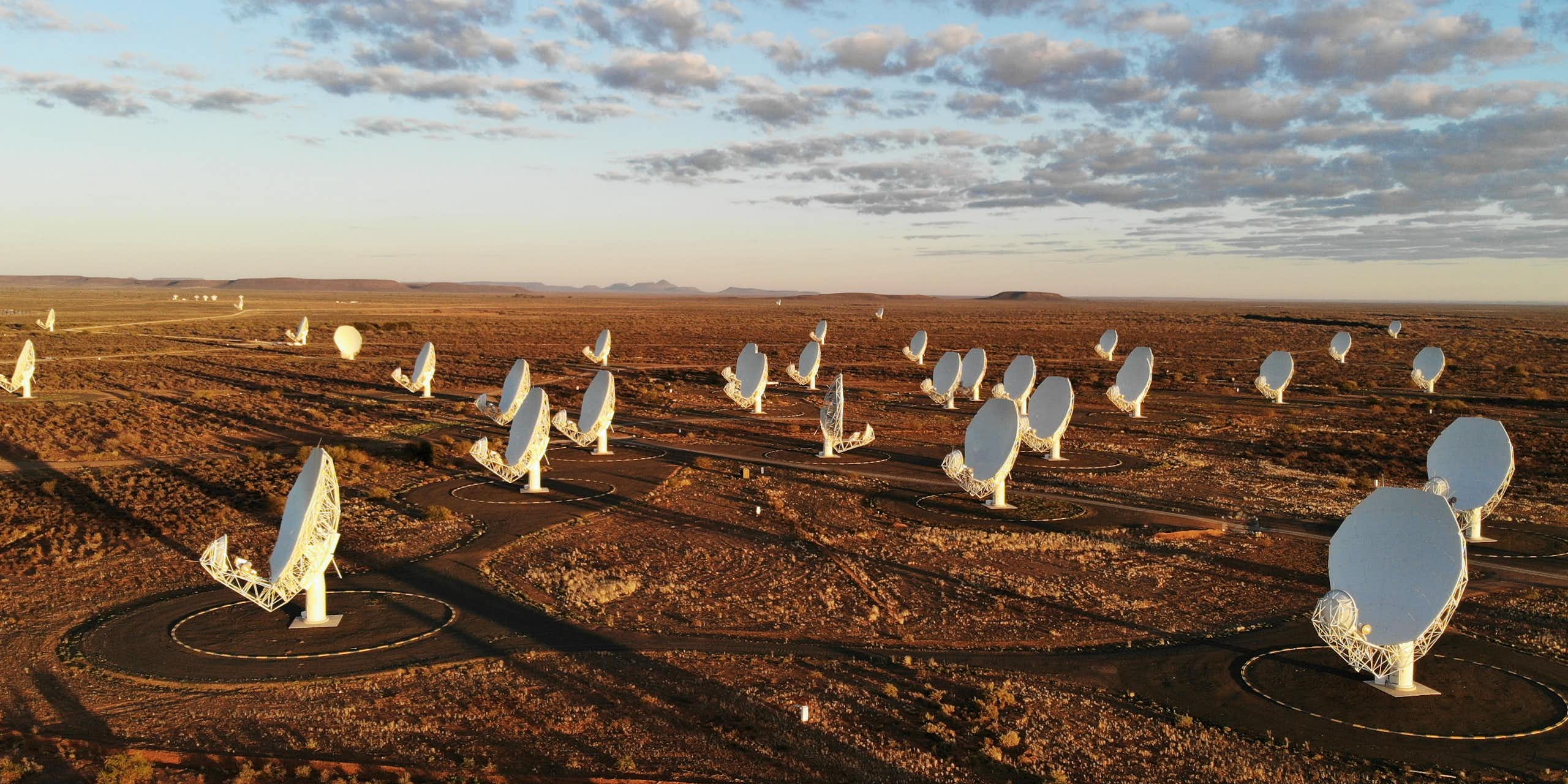 Large white satellite dishes, their receivers pointed up to the sky, are photographed in a sprawling, empty patch of land