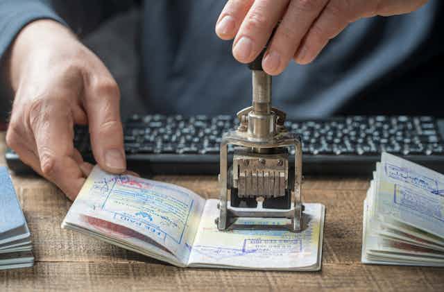 Close up photo of the hands of a border control officer putting a stamp in a passport