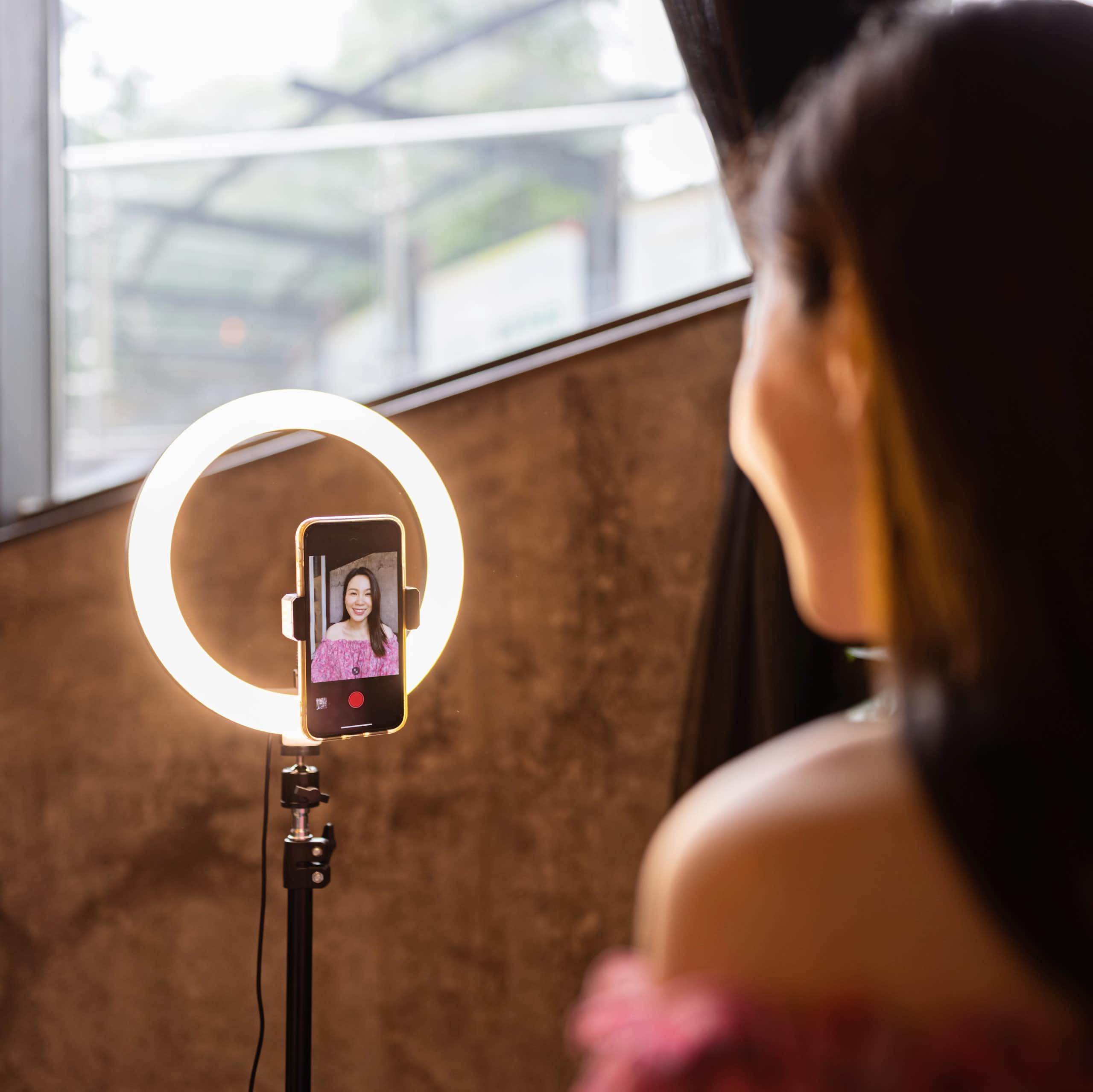An influencer users her phone and a ring light to film.