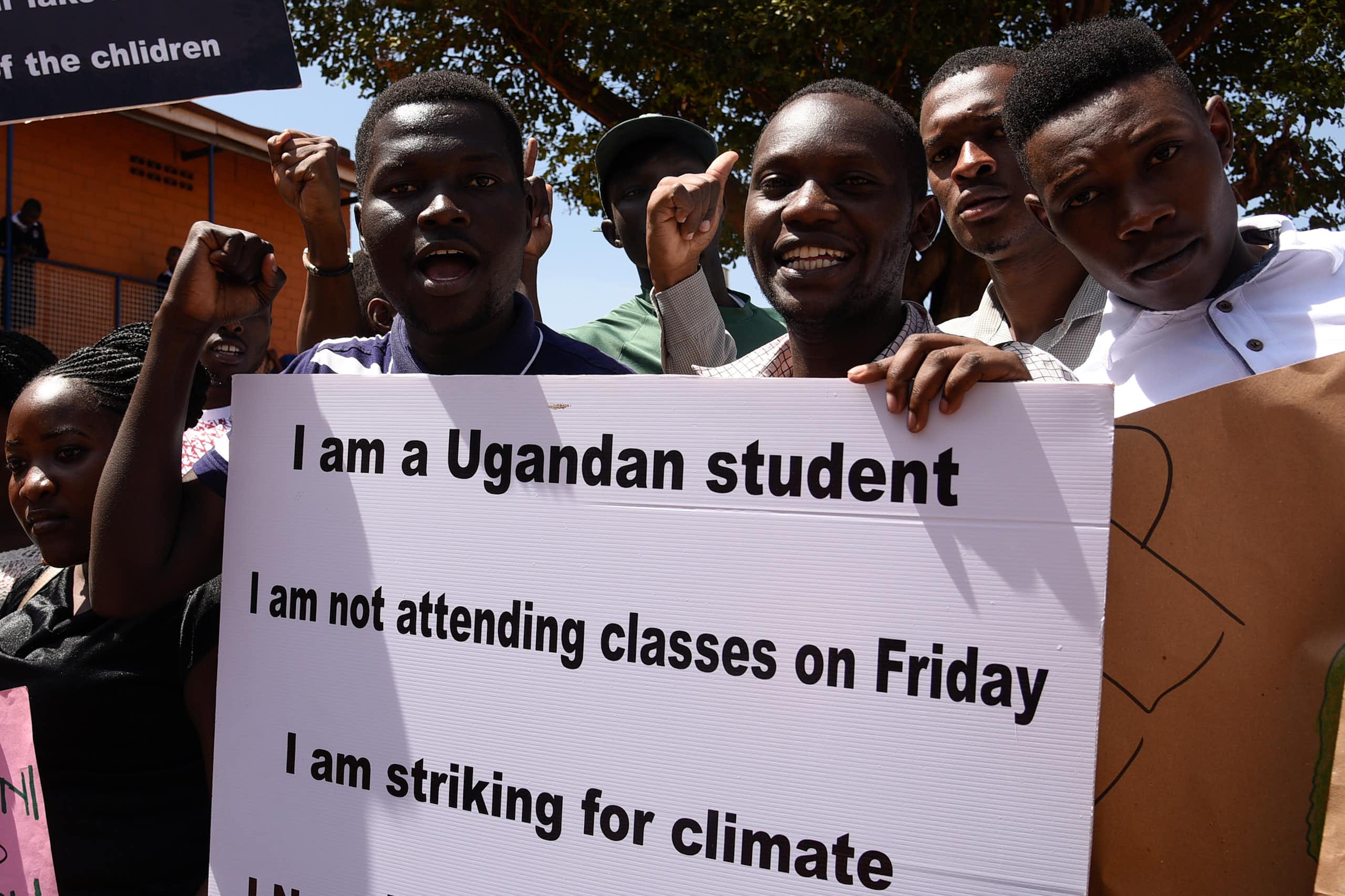 A young man holds up a placard that reads "I am a Ugandan student I am not attending classes on Friday I am striking for climate". He is surrounded by others who are raising their fists or holding similar placards