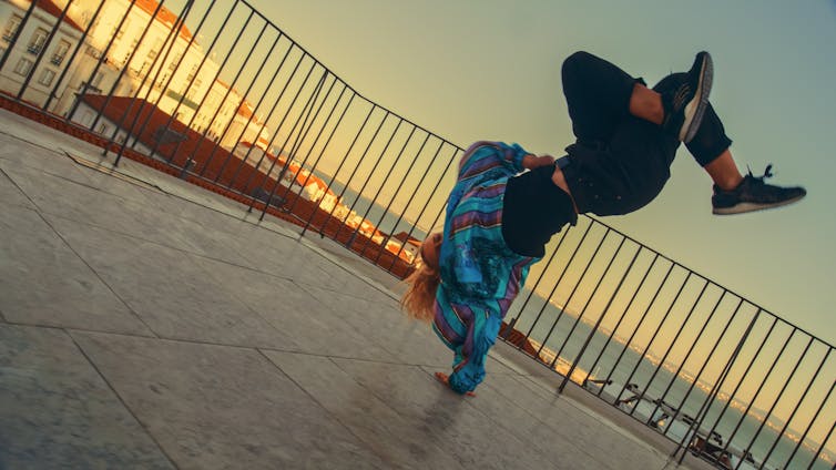 A young girl breakdancing on a roof terrace.