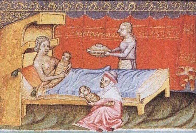 Una mujer abraza a un bebé en la cama mientras otra mujer sentada al lado abraza a otro bebé.