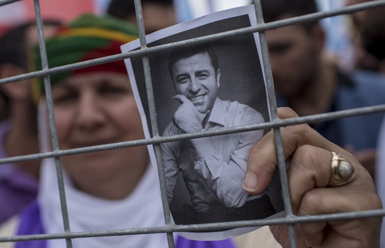 A women holding a picture of a man through a fence.
