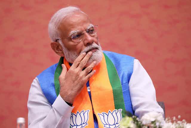 Narendra Modi sat in colourful attire stroking his beard.