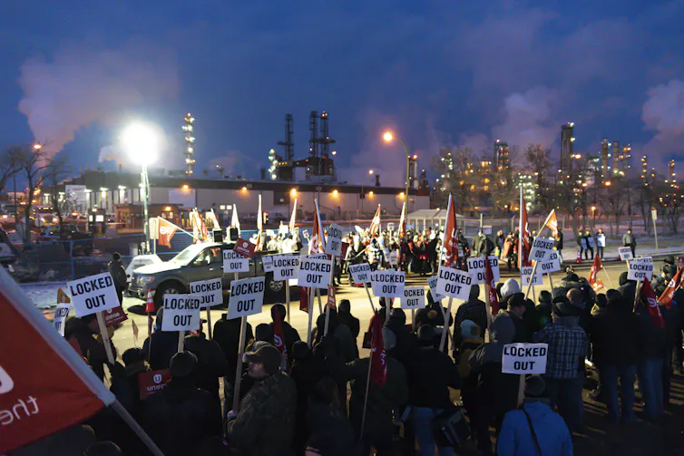 A crowd of people holding signs stand on a picket line.