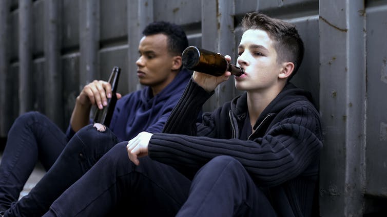 Two young boys sitting on the floor, drinking beer