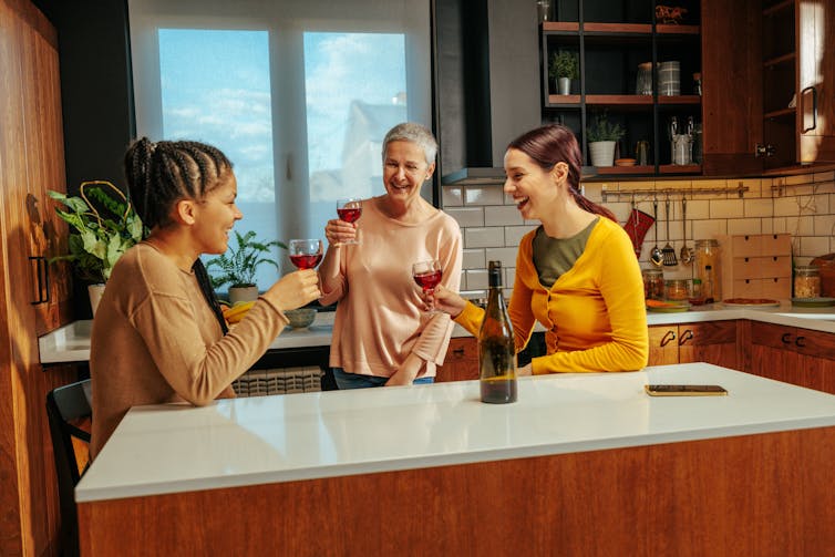 Three women, one of them older, drinking wine, standing in a kitchen